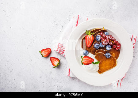 Pfannkuchen in der Form eines Herzens mit Beeren, Obst und Quark Sahne in eine weiße Platte, Ansicht von oben. Valentinstag Konzept. Stockfoto