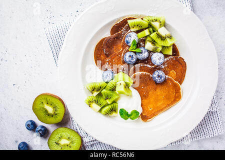 Pfannkuchen in der Form eines Herzens mit Beeren, Obst und Quark Sahne in eine weiße Platte, Ansicht von oben. Valentinstag Konzept. Stockfoto