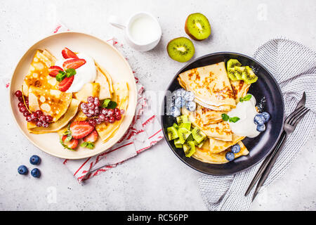 Hausgemachte dünne Crepes mit Quark Sahne, Früchten und Beeren in Schwarz und Weiß Teller serviert. Gesunde schöne Frühstück Konzept. Stockfoto