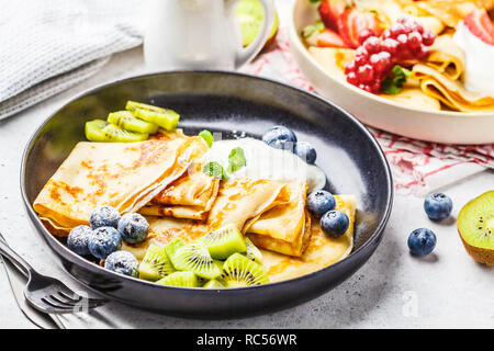 Hausgemachte dünne Crepes mit Quark Sahne, Früchten und Beeren in Schwarz und Weiß Teller serviert. Gesunde schöne Frühstück Konzept. Stockfoto