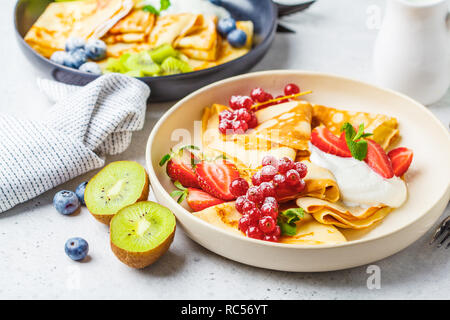Hausgemachte dünne Crepes mit Quark Sahne, Früchten und Beeren in Schwarz und Weiß Teller serviert. Gesunde schöne Frühstück Konzept. Stockfoto