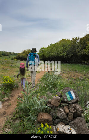 Ein israelischer Vater, der mit ihrer Tochter in Golan Heights wandert. Das Logo des berühmten 'Golan Trail' ist im Vordergrund zu sehen. Stockfoto