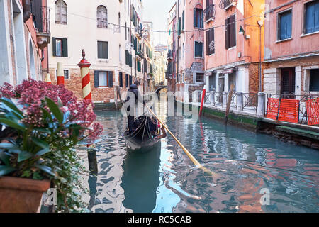 Venedig, Italien - 10. Februar 2018: gondoliere Fahrten Gondel durch den schmalen Kanal zwischen bunten historischen Häusern an einem sonnigen Wintertag Stockfoto