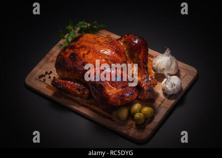 Ganzen gebratene Hähnchen auf Schneidebrett mit Gemüse auf schwarzen Hintergrund. Stockfoto
