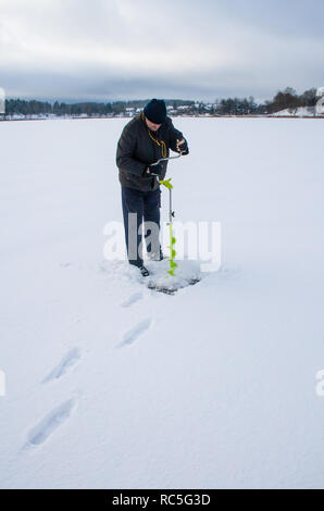 Man Bohrungen Eis mit Bohrer für Angeln im Winter verschneite Morgen, gefrorenen See, vertikal Stockfoto