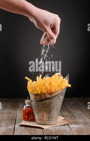 Hand streut Salz auf Pommes Frites Stockfoto