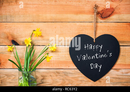 Happy Valentine's Tag auf einer Schiefertafel in der Form eines Herzens, Narzissen und Holzbohlen Hintergrund Stockfoto