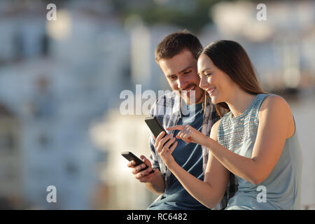 Glückliches Paar sharing smart phones Inhalt in einer Stadt Stadtrand im Urlaub Stockfoto