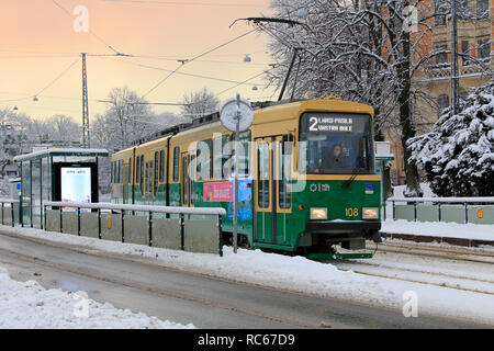 Helsinki, Finnland - 9. Januar 2019: Grüne HSL die Straßenbahn Nr. 2 fährt von der Haltestelle an einem schönen Tag der Winter mit Schneefall in Helsinki. Stockfoto