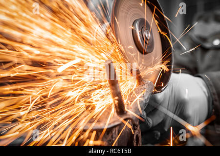 Nahaufnahme eines Mannes sägen Metall Lager mit einer Handkreissäge, helle Blitze fliegen in verschiedenen Richtungen, im Hintergrund Tools für ein Auto Stockfoto