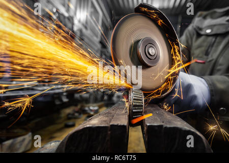 Eine Nahaufnahme von einem Automechaniker mit einem Metall Grinder Lager in einer Werkstatt zu schneiden, helle Blitze fliegen in verschiedene Richtungen. Die Arbeit der Aut. Stockfoto