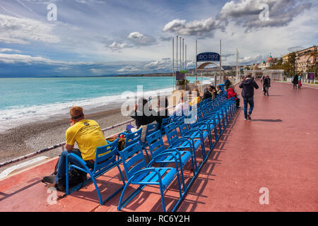 Stadt Nizza in Frankreich, Menschen entspannen am Meer an der Promenade des Anglais und blaue Stühle auf Französische Riviera - Cote d'Azur Stockfoto