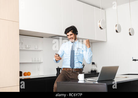 Zuversichtlich, dass junge Unternehmer zu Hause in der Küche arbeiten, mit Laptop Computer, Kommunikation über Kopfhörer Stockfoto