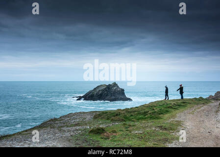 Zwei Personen stehen auf Pentire Punkt Osten Blick auf die Gans eine kleine felsige unbewohnte Insel vor der Küste von Cornwall Newuay. Stockfoto