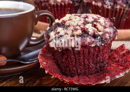 Nahaufnahme von einem roten Samt Chocolate Chip Muffin und Tasse Kaffee auf einer hölzernen Oberfläche Stockfoto