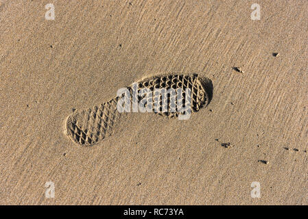 Ein Abdruck einer Shoeprint in feuchten Sand am Strand. Stockfoto