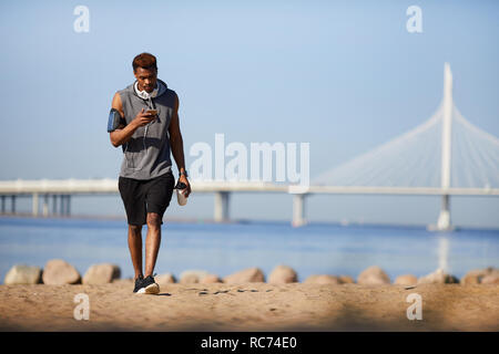Schwere schwarze Kerl sms sms beim Gehen auf den Strand Stockfoto