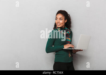 Fröhlich afrikanische Frau mit Kopftuch stehend über grauen Hintergrund isoliert, Laptop Stockfoto