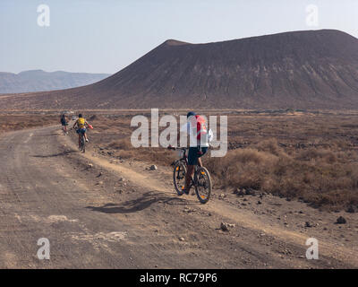 Menschen Radfahren auf einem unbefestigten Pfad in der Insel La Graciosa, Lanzarote, Kanarische Inseln. Spanien. Im Hintergrund El Risco, Lanzarote Berg Stockfoto