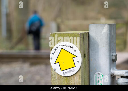 Nahaufnahme von großen, gelben Pfeil öffentlichen Fußweg Zeichen genagelt, Outdoor, Land gatepost. Ansicht der Rückseite des einzelnen Mann im Hintergrund auf Wald Weg. Stockfoto