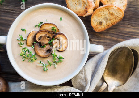 Cremige Pilzsuppe mit Champignons auf rustikalen Holzmöbeln Hintergrund. Ansicht von oben. Stockfoto