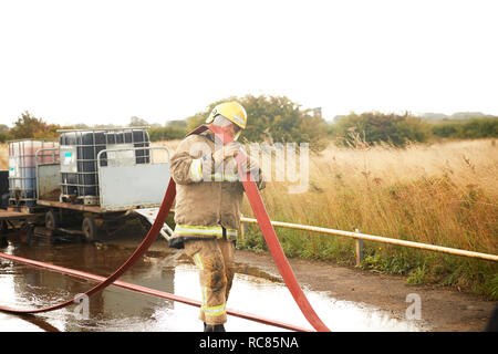 Feuerwehr Training, Feuerwehrmann mit löschschlauch über seine Schulter zu Training Service Stockfoto