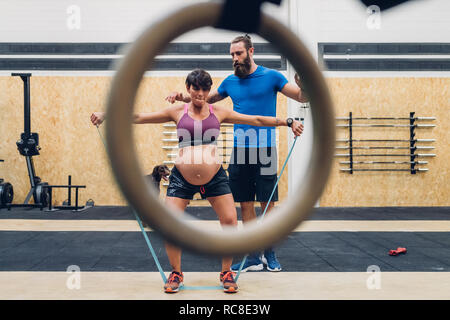 Trainer führen schwangere Frau mit Hilfe von Seilen in der Turnhalle Stockfoto