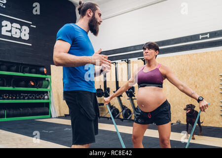 Trainer führen schwangere Frau mit Hilfe von Seilen in der Turnhalle Stockfoto