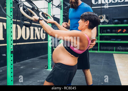 Trainer führen schwangere Frau mit Trainingsgeräten in der Turnhalle Stockfoto