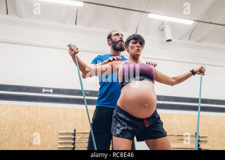 Trainer führen schwangere Frau mit Hilfe von Seilen in der Turnhalle Stockfoto