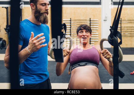 Trainer führen schwangere Frau mit Trainingsgeräten in der Turnhalle Stockfoto