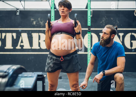 Trainer führen schwangere Frau mit Gewichten in der Turnhalle Stockfoto