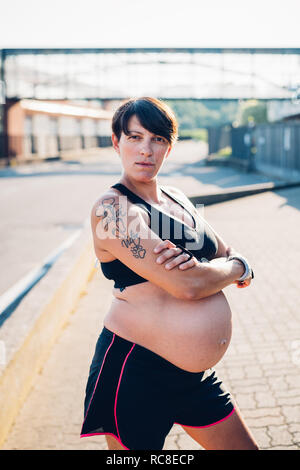 Schwangere Frau in sportklamotten im Sonnenschein Stockfoto