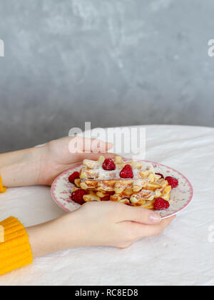 Selbst gebackene Waffeln mit Himbeeren in das Mädchen Hände auf dem Tisch Stockfoto