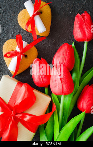 Romantische Komposition für Valentinstag, Geburtstag oder Muttertag. Geschenkbox, Kekse in der Form eines Herzens mit einem Hinweis und roten Tulpen. Stockfoto