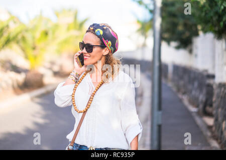 Trendige Mode und Konzepte. Close-up Portrait von glücklichen Farbigen lächelnde junge Frau mit einem Handy in der Straße mit Straßen und Anlagen in der Ba Stockfoto
