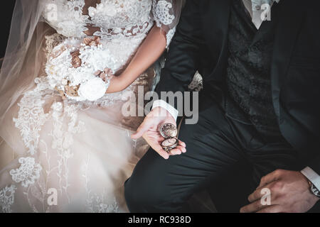 Schön frisch vermählte Paar. Braut hält wedding bouquet, während der Bräutigam bei alte Taschenuhr suchen. Vintage Style Foto. Stockfoto