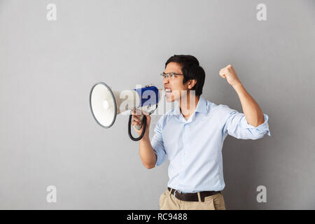 Wütend Asian Business Mann stehend über grauer Hintergrund isoliert, an einen Lautsprecher schreien Stockfoto
