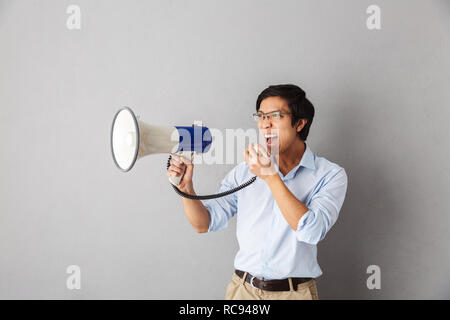 Wütend Asian Business Mann stehend über grauer Hintergrund isoliert, an einen Lautsprecher schreien Stockfoto