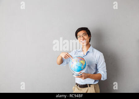 Happy Asian Business Mann stehend über grauer Hintergrund isoliert, holding Earth Globus Stockfoto