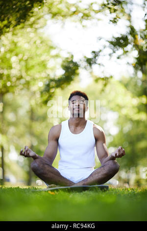 Ernsthafte schwarzer Mann mit gekreuzten Beinen Meditation in Park Stockfoto