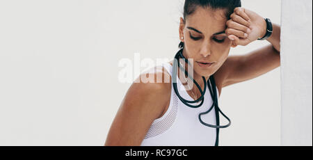 Sportlerin eine Pause vom Training stand neben einer Wand. 7/8 Schuß eines athletischen Frau entspannende während des Trainings mit einem Springseil auf Er Stockfoto