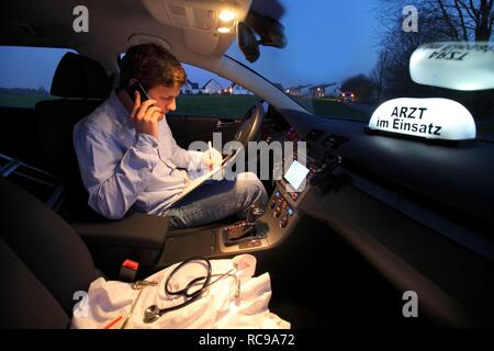 Junge GP, Arzt für Allgemeinmedizin im Land arbeiten, Anruf und ist die, die sich Notizen in seinem Auto nach einem Abend home Stockfoto