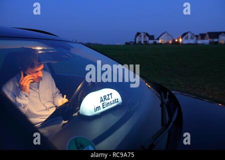 Junge GP, Arzt für Allgemeinmedizin im Land arbeiten, Anruf und ist die, die sich Notizen in seinem Auto nach einem Abend home Stockfoto