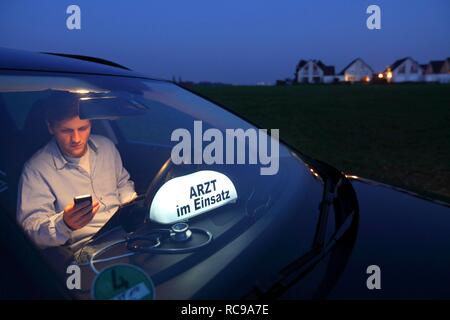 Junge GP, Arzt für Allgemeinmedizin im Land arbeiten, die Anruf in seinem Auto nach einem Abend zu Hause besuchen, Auto anzeigen Stockfoto
