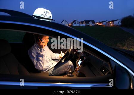 Junge GP, Arzt für Allgemeinmedizin im Land arbeiten, die anrufen und sich Notizen in seinem Auto nach einem Abend home Stockfoto