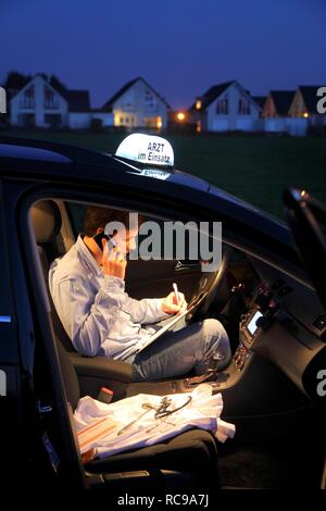 Junge GP, Arzt für Allgemeinmedizin im Land arbeiten, die anrufen und sich Notizen in seinem Auto nach einem Abend home Stockfoto