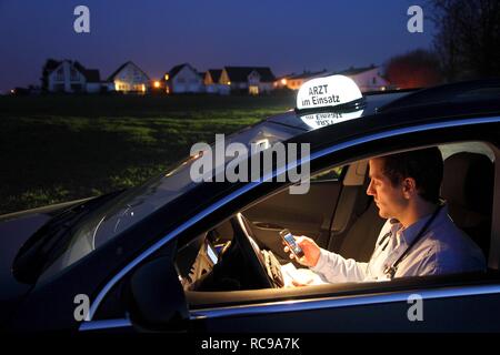 Junge GP, Arzt für Allgemeinmedizin im Land arbeiten, die anrufen und sich Notizen in seinem Auto nach einem Abend home Stockfoto
