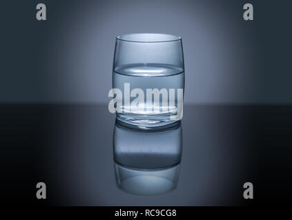 Glas mit Wasser auf reflektierenden Tabelle auf dunklem Hintergrund mit Spotlight Stockfoto