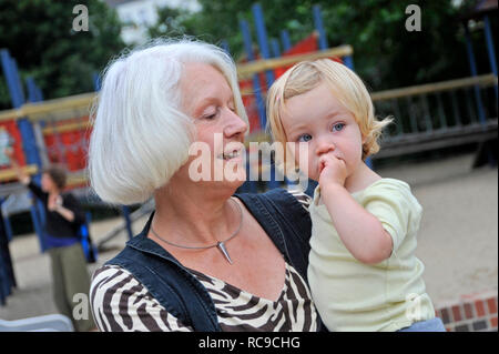 Oma auf dem Spielplatz hat Enkelkind im Arm | Großmutter trägt ihre Enkelin auf dem Arm Stockfoto